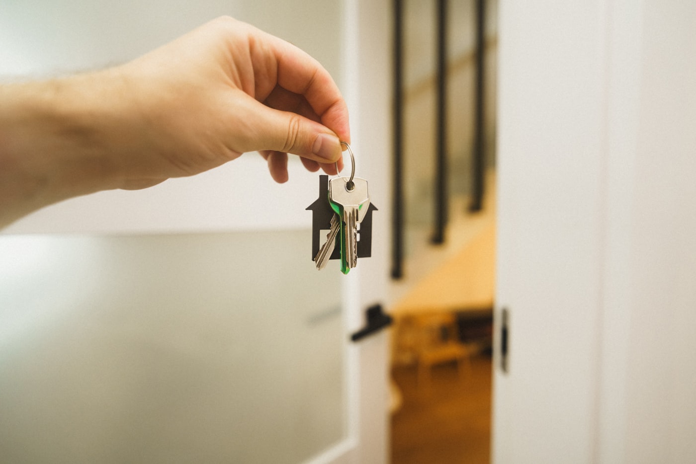 A hand holding out house keys with a house-shaped keychain in an open doorway.